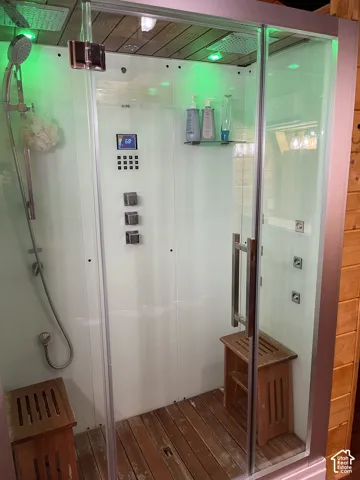 Glass-enclosed shower with wood-finish flooring, integrated shower jets, and a digital control panel