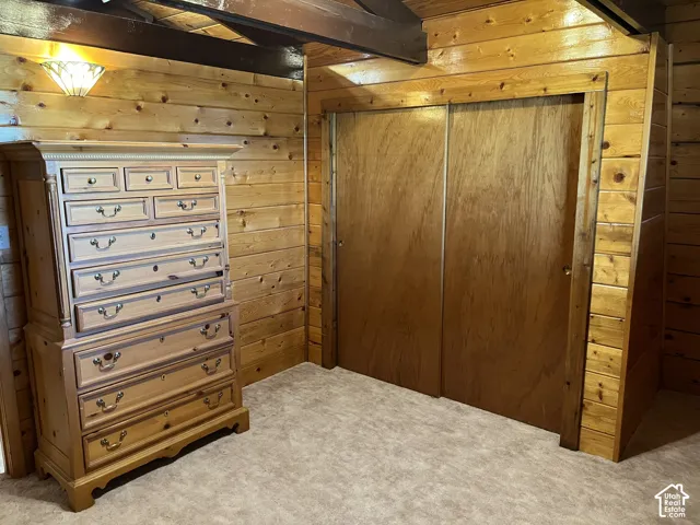 Pine wood paneling, sliding closet doors, wall-mounted light fixture, wood-finish ceiling beam, carpet flooring