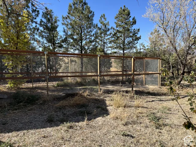 Wood-framed enclosure with mesh panels, surrounded by mature trees and natural landscaping