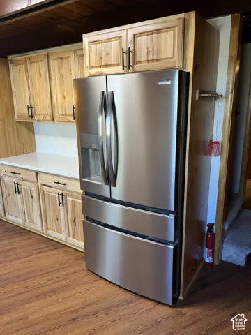 Stainless steel French door refrigerator, wood-finish flooring, light wood cabinetry with dark hardware, white countertops, and a white tile backsplash