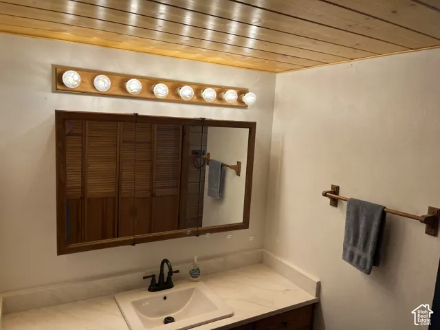 Wood-paneled ceiling, vanity with an integrated sink and countertop, framed mirror, and a multi-bulb light fixture
