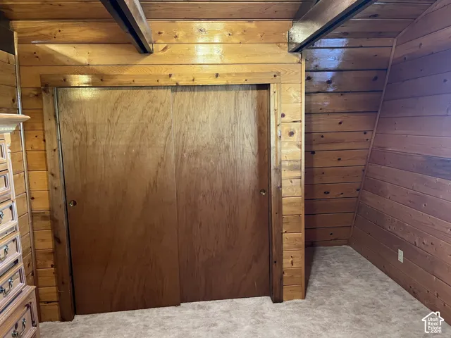 Wood-paneled walls and ceiling beams, with a built-in closet featuring sliding wood doors and a neutral-toned carpet