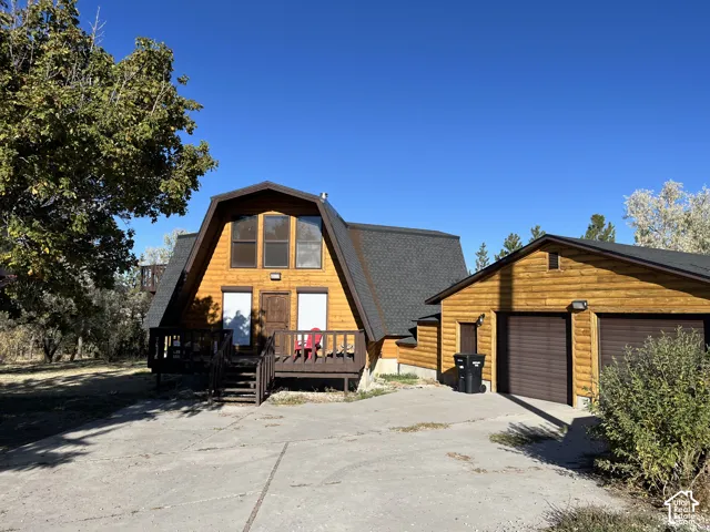 A-frame architectural style with wood siding, a dark shingle roof, a front-facing deck, and an attached two-car garage