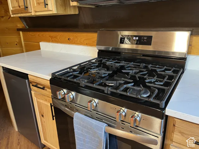 Stainless steel range with gas burners, white countertops, natural wood-finish cabinetry, and a built-in dishwasher