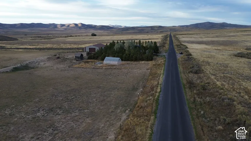 Rural property featuring a long paved road, distant mountains, and a large metal-sided building with a roll-up door