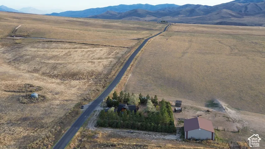 Expansive rural property featuring a long paved road, mature trees, a detached barn, and distant mountain ranges