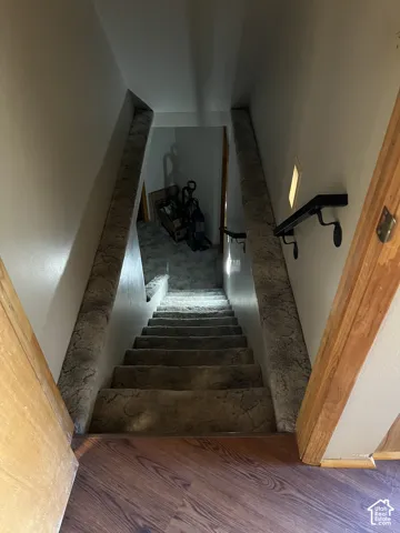 Wood-finish flooring with a textured carpeted staircase, featuring a black wall-mounted handrail and recessed lighting