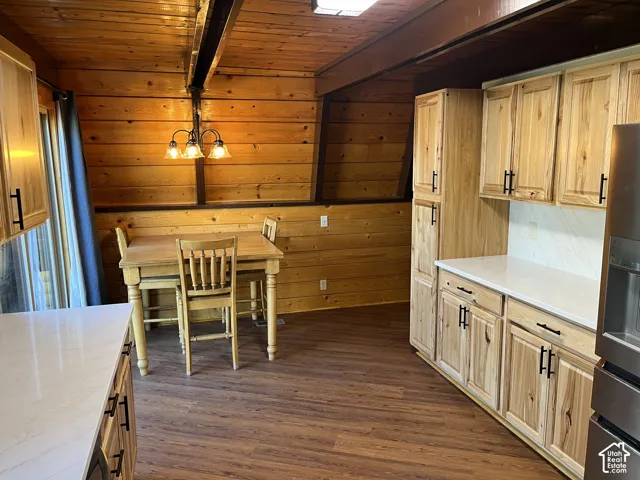 Wood-paneled walls and ceiling with exposed beam, wood-finish flooring, light wood cabinetry with black hardware, white countertops, and a white tile backsplash