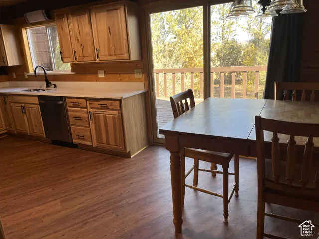 Wood-finish flooring throughout, wooden cabinetry with dark hardware, a black sink with a matching faucet, a built-in dishwasher, and a sliding glass door leading to a wooden deck