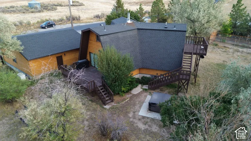 Dark shingle roofing with a prominent chimney, wood-sided exterior, spacious wood-finish deck with stairs, built-in outdoor spa, and an additional elevated wood-finish deck
