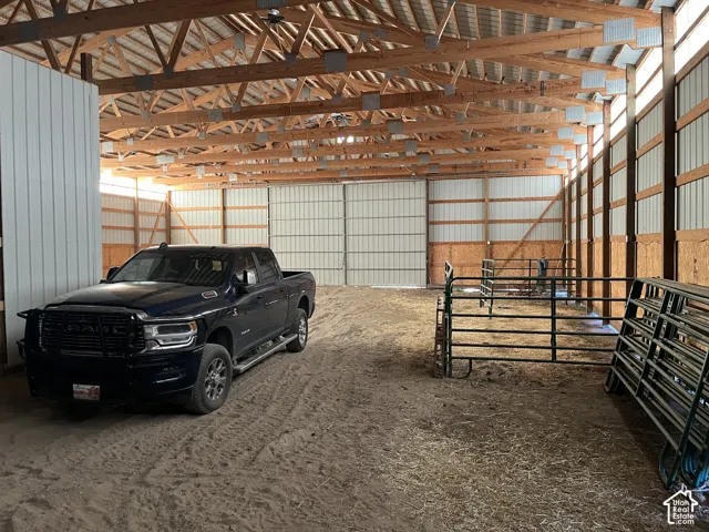 Spacious interior barn with exposed wood beam construction, corrugated metal siding, large overhead doors, and multiple light fixtures
