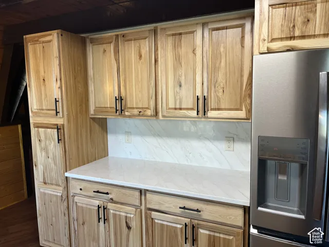 Custom wood cabinetry with black hardware, stainless steel refrigerator with dispenser, white solid surface countertop, and a white patterned backsplash
