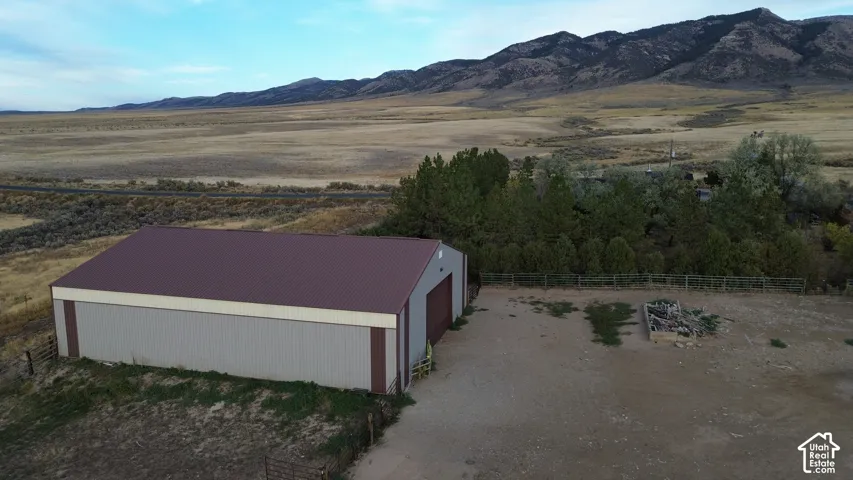 Metal outbuilding with a maroon roof, large driveway, and distant mountainous terrain