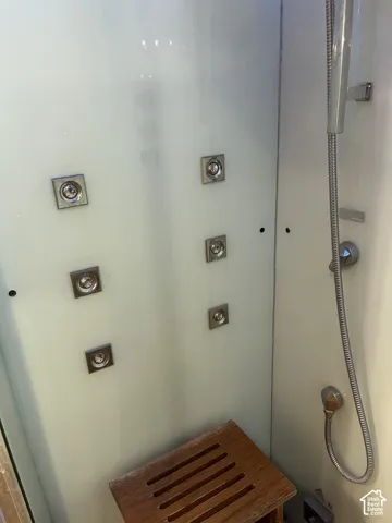 Shower enclosure featuring multiple body jets, a handheld shower head, and an integrated wood-finish bench