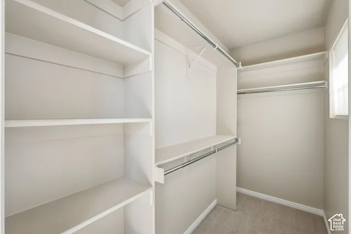 Walk-in closet featuring built-in shelving, multiple hanging rods, and light-colored carpeting