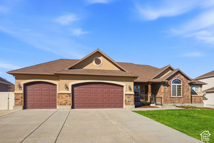 Stucco exterior with stone accents, two attached garages, arched garage doors, a curved bay window, and a concrete driveway