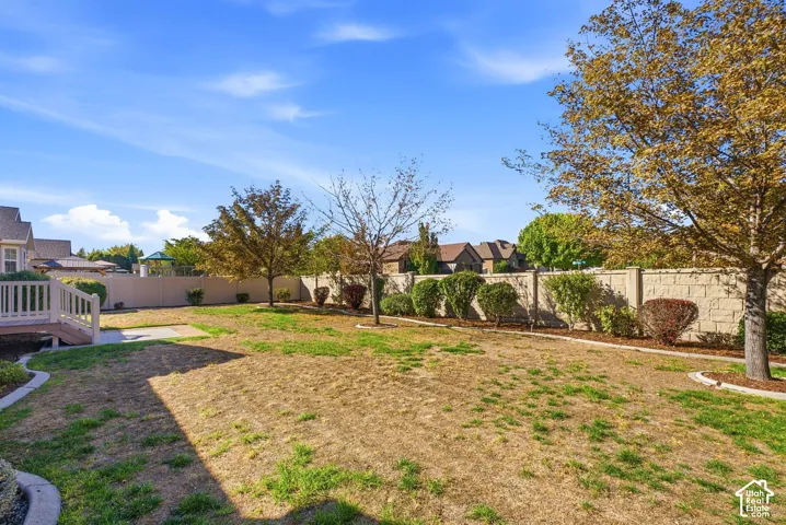 Spacious backyard featuring a stone privacy wall, mature trees, and a raised wood deck with railings