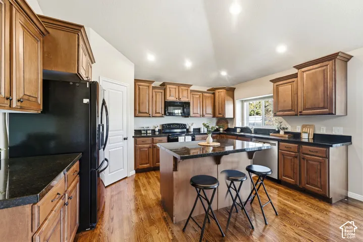 Kitchen featuring wood-finish flooring, dark stone countertops, wood cabinetry, a central island with seating, and recessed lighting
