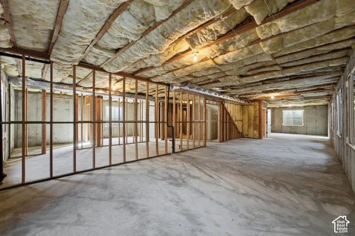 Unfinished basement with concrete flooring, exposed ceiling insulation, wood framing, and windows