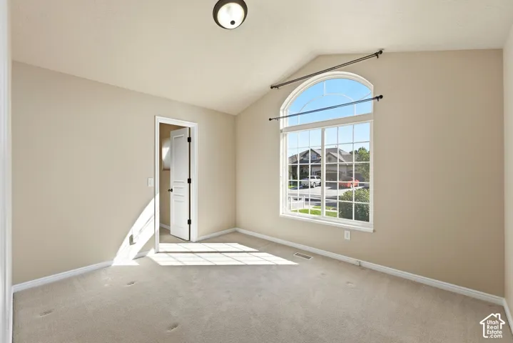 Vaulted ceiling, arched window, carpeted flooring, and a flush-mount light fixture