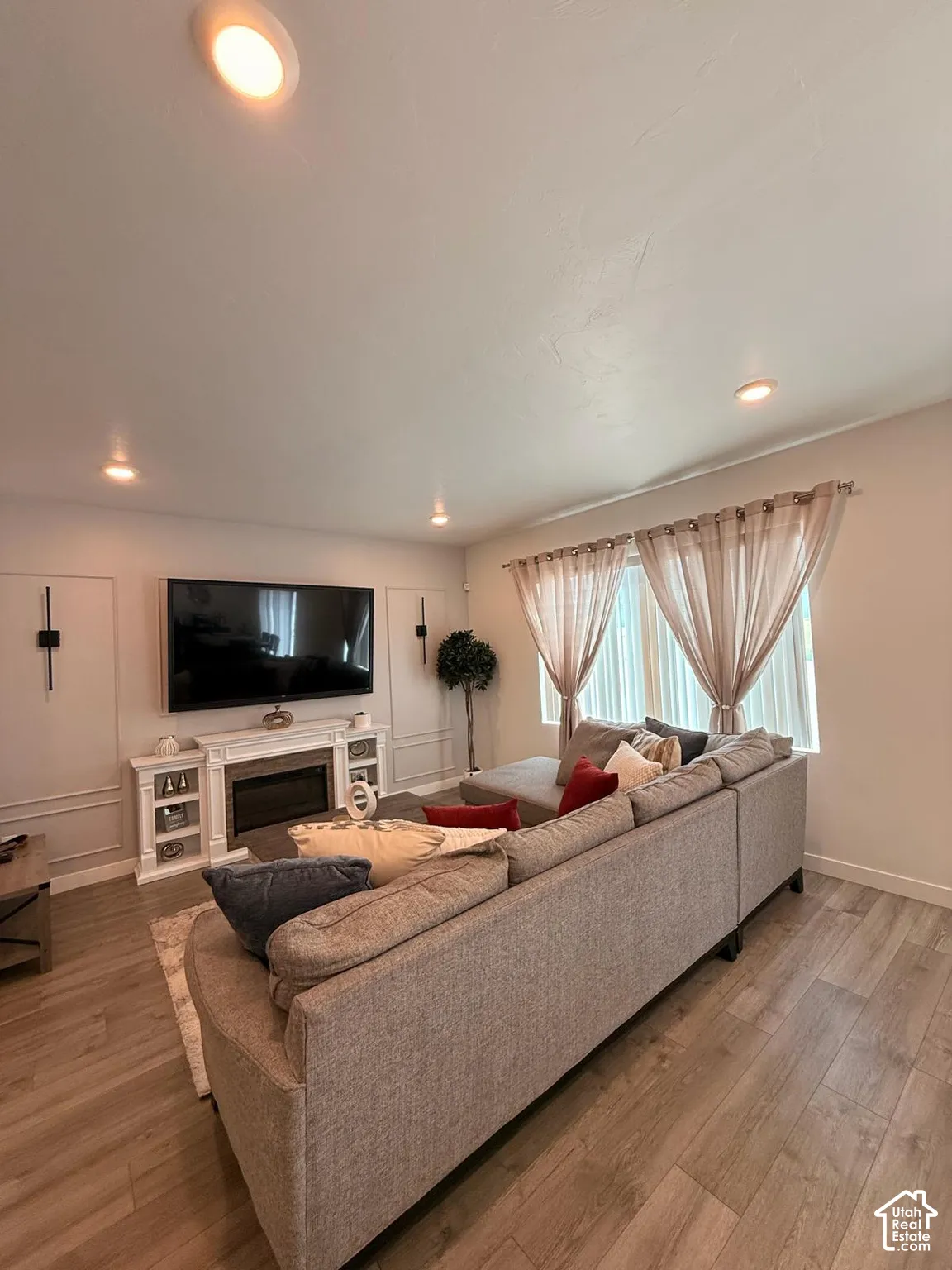 Recessed lighting, wood-finish flooring, white fireplace surround with built-in shelving, decorative wall molding, and large windows