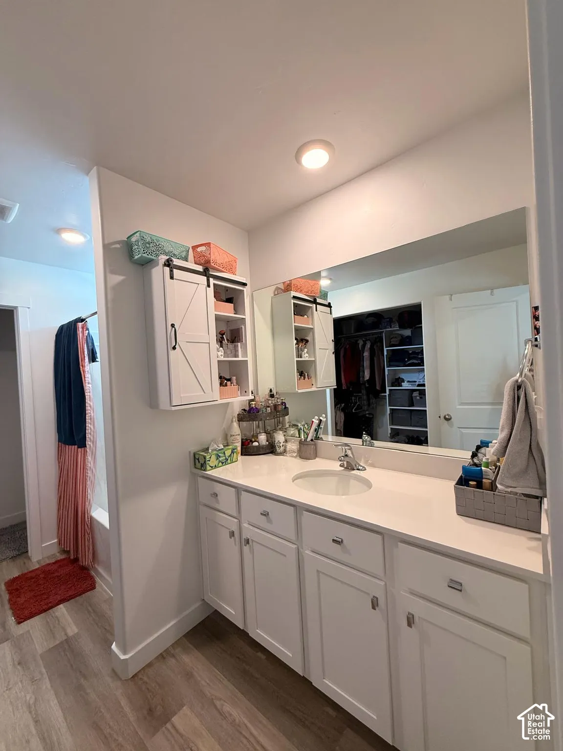 White vanity with integrated sink, expansive countertop, large mirror, and wood-finish flooring