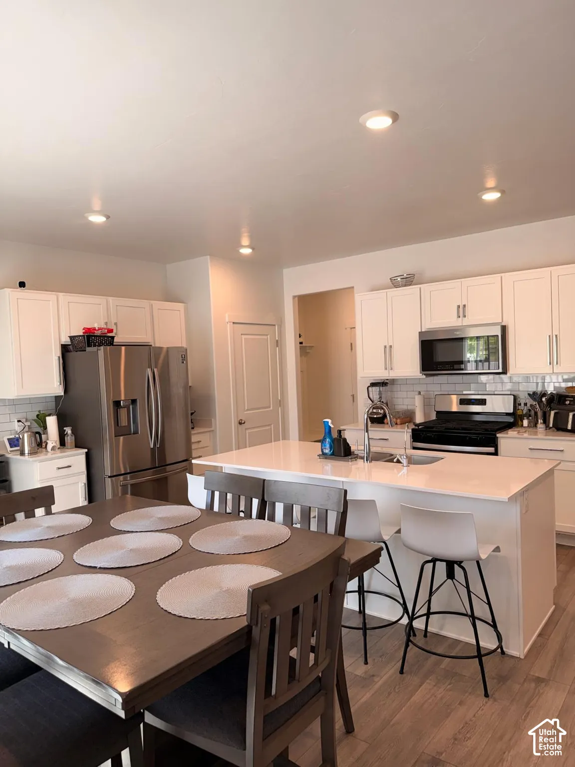 Kitchen featuring white cabinetry, stainless steel appliances, a center island with seating, and wood-finish flooring