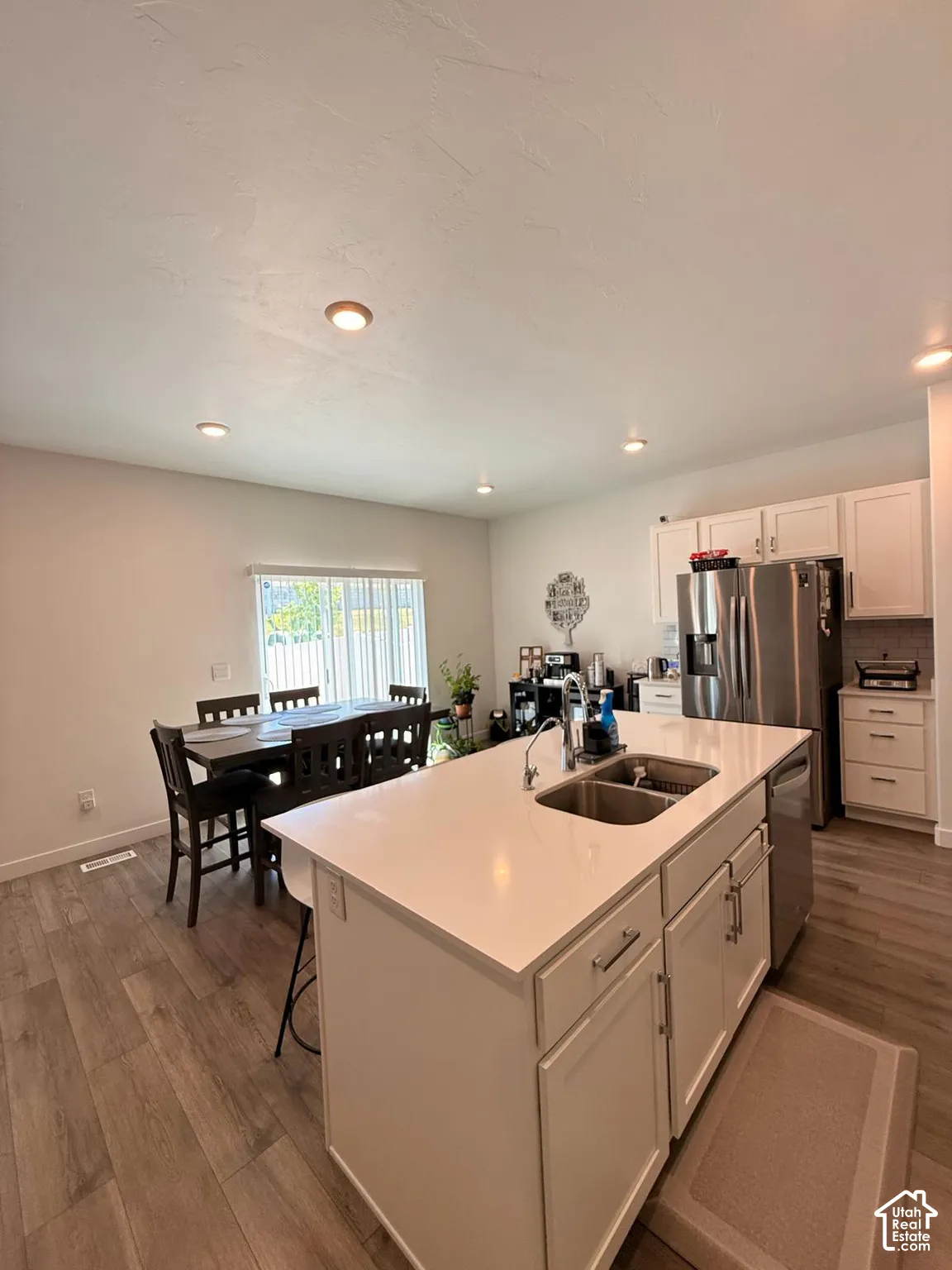 Kitchen featuring a center island with double basin sink, stainless steel appliances, white cabinetry, and wood-finish flooring