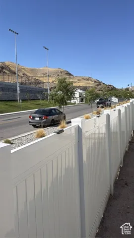 White privacy fencing borders a landscaped street with decorative gravel and small trees