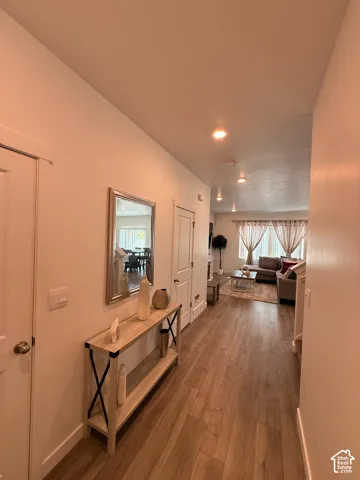 Wood-finish flooring extending through the hallway and living area, with recessed lighting throughout