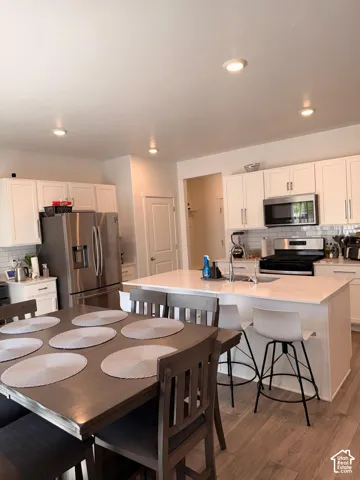 Kitchen featuring white cabinetry, stainless steel appliances, a center island with seating, and wood-finish flooring