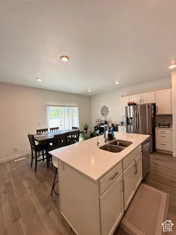 Kitchen featuring a center island with double basin sink, stainless steel appliances, white cabinetry, and wood-finish flooring
