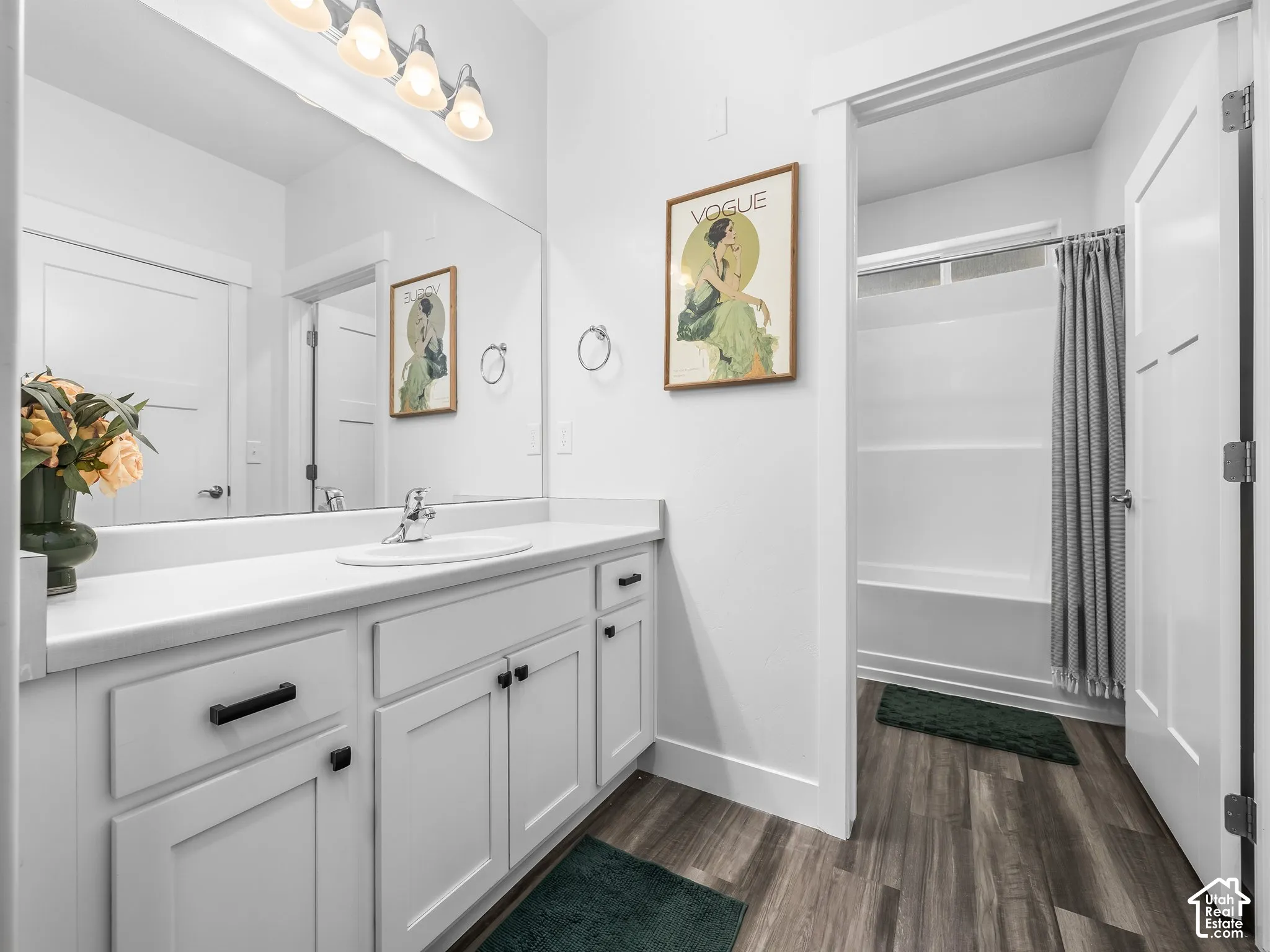 Spacious bathroom featuring a single vanity with extensive countertop space, white cabinetry, and wood-finish flooring