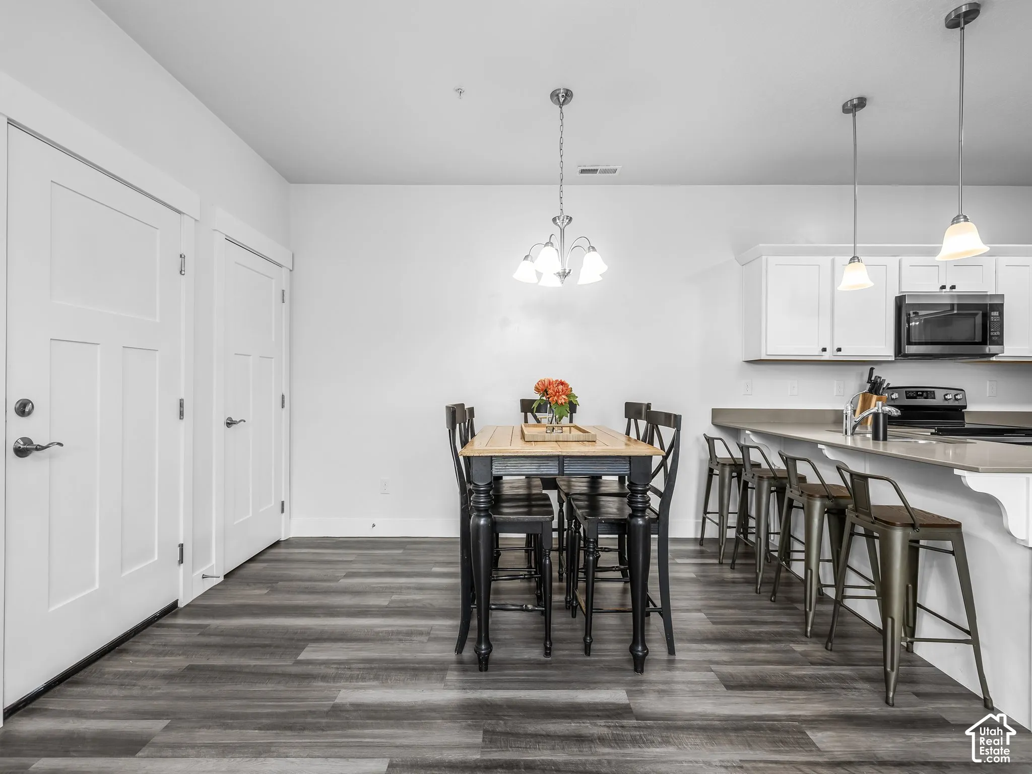 Wood-finish flooring throughout, white shaker-style cabinetry, stainless steel appliances, pendant lighting, and a kitchen island with seating
