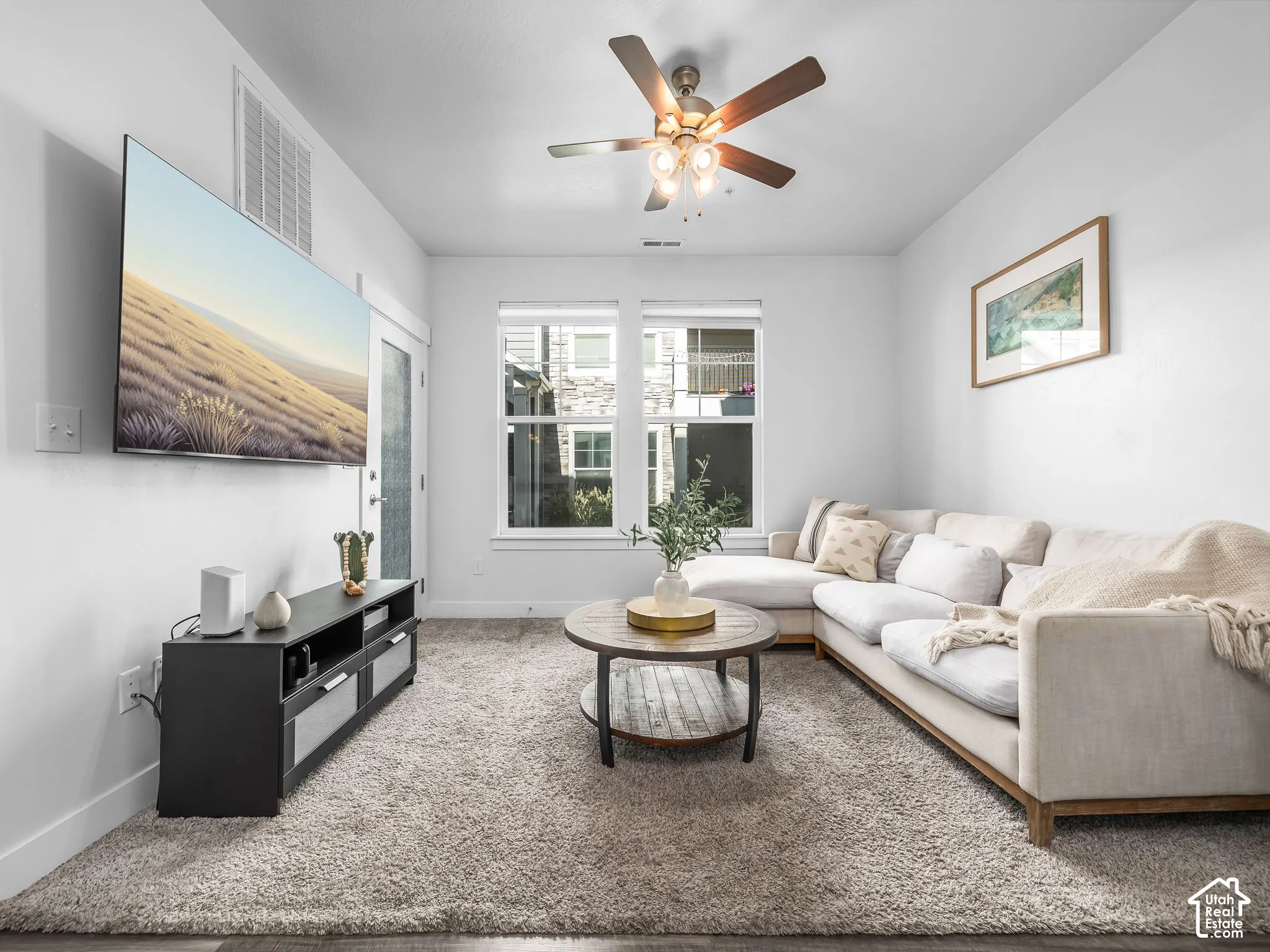 Bright living space featuring a ceiling fan with light fixture, large window, and light-colored carpeting