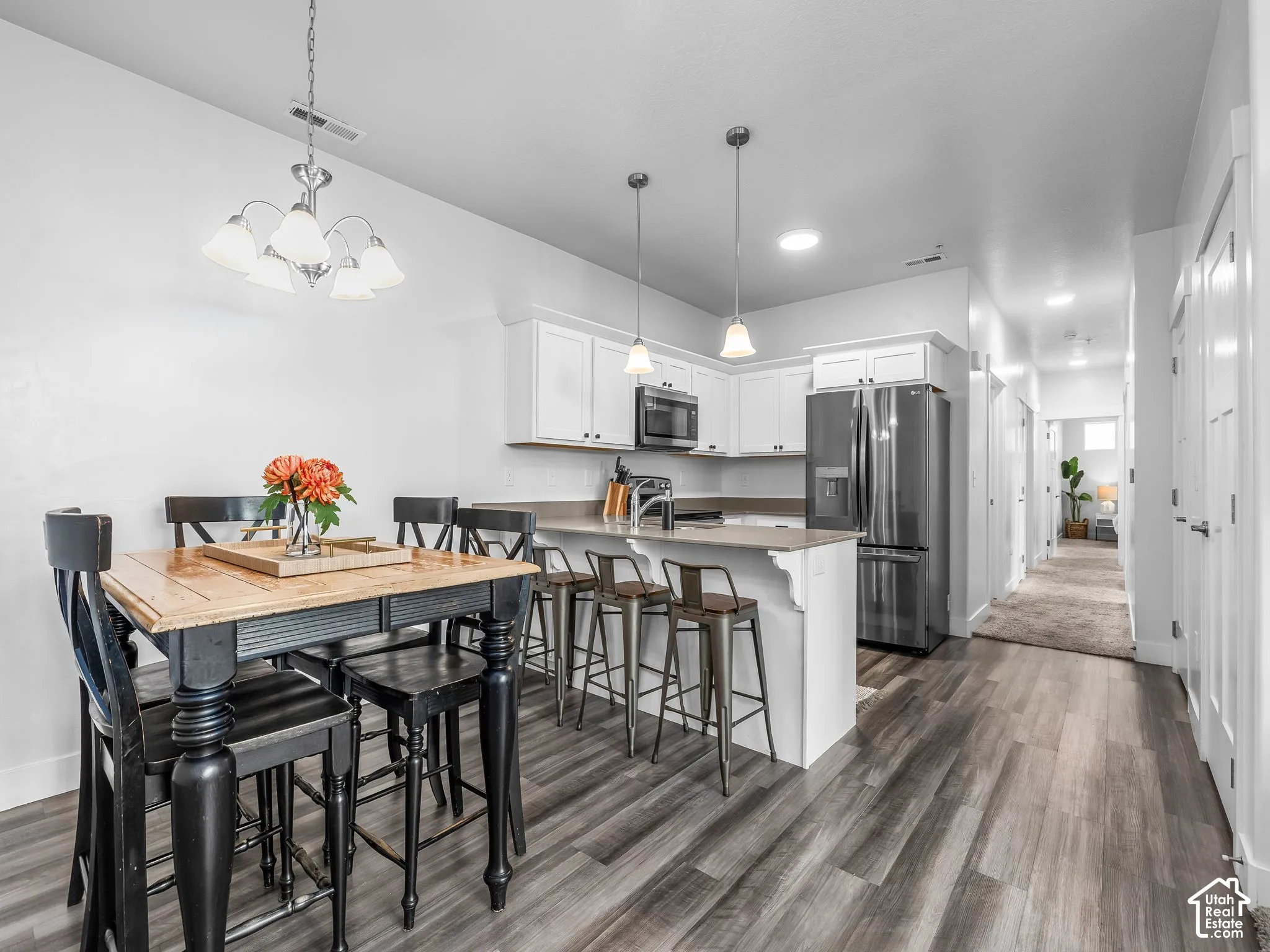 Open-concept kitchen featuring white cabinetry, stainless steel appliances, a breakfast bar, and wood-finish flooring