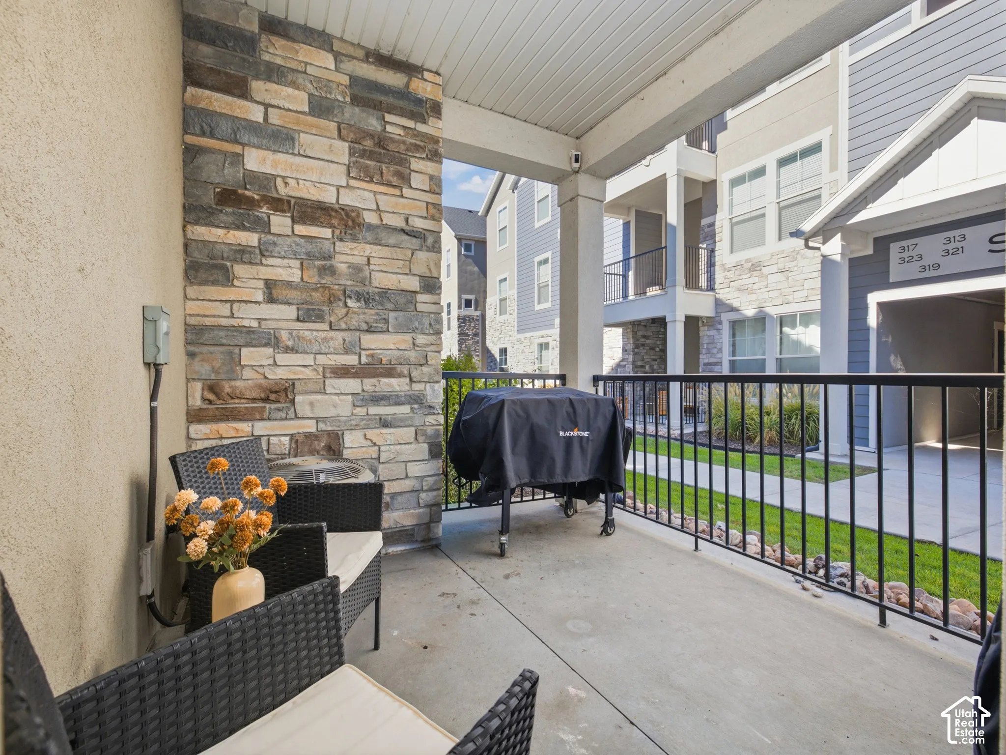 Covered patio with a concrete surface, stone veneer accent wall, and black metal railing