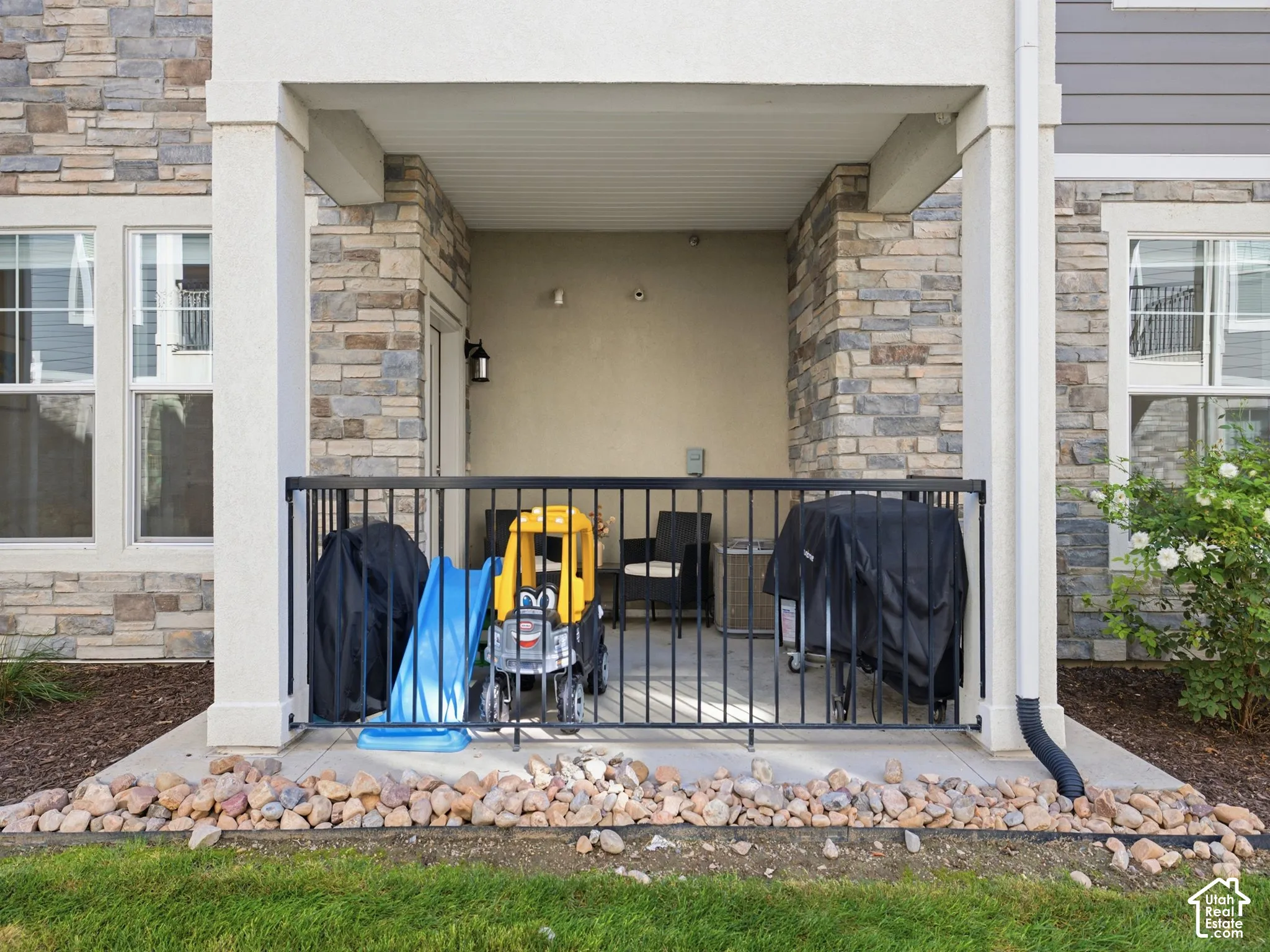 Covered patio with a concrete floor, black metal railing, and stone veneer accents