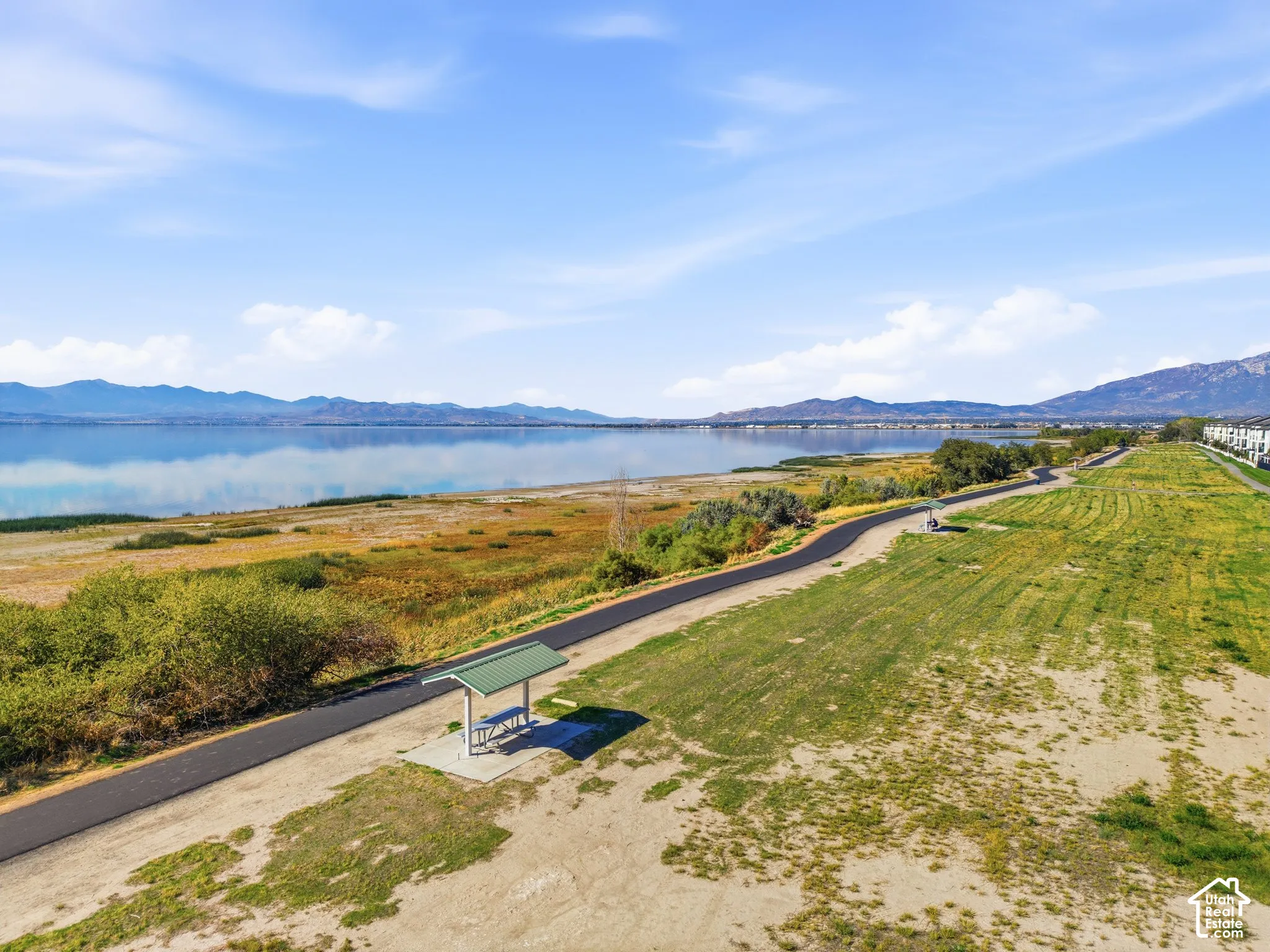 Waterfront property with a paved pathway, expansive grassy area, and a picnic shelter