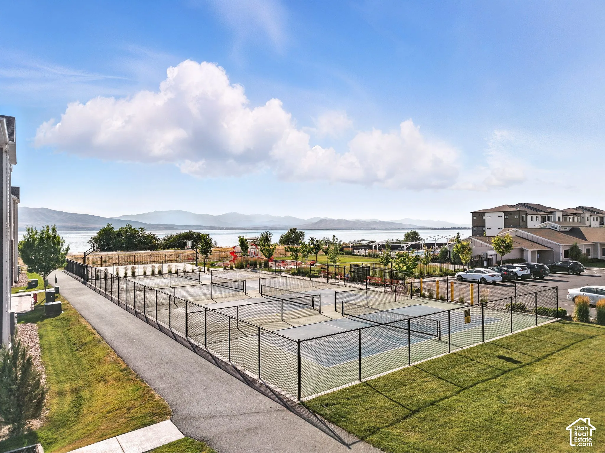 Multiple hard-surface courts with fencing, paved walkways, landscaped grounds, and a mountain and water backdrop