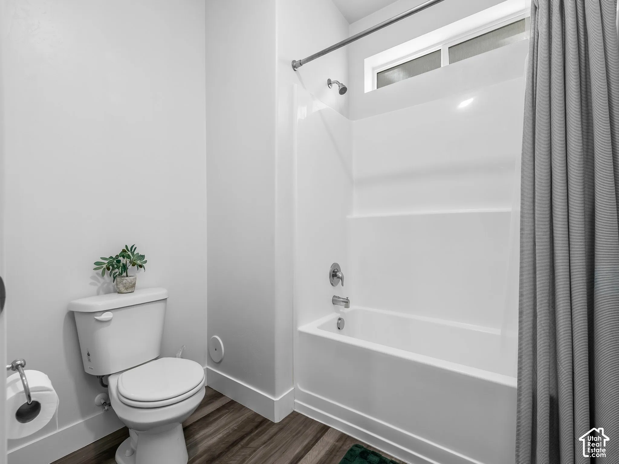 White tub and shower combination with chrome fixtures, wood-finish flooring, and white baseboards