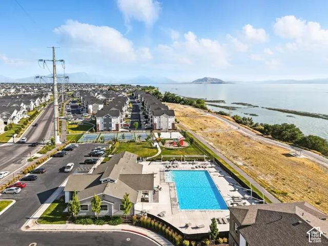 Expansive outdoor swimming pool with surrounding lounge areas, integrated tennis courts, playground area, and a large body of water in the background
