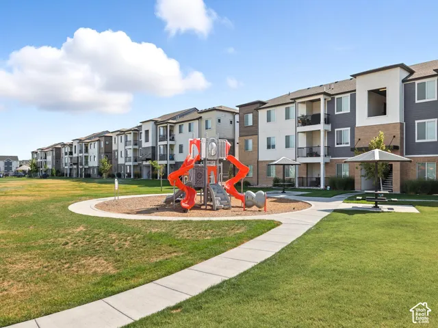 Expansive grassy area featuring a playground, curved concrete pathway, and covered picnic area with seating