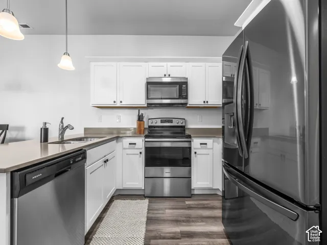 Kitchen featuring stainless steel appliances, white cabinetry, wood-finish flooring, and pendant lighting