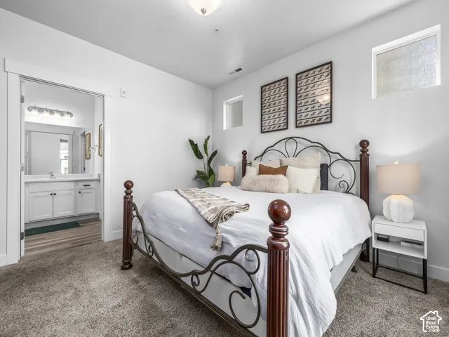 Recessed lighting, two high windows, textured carpeting, and a doorway to an attached bathroom featuring a vanity with white cabinetry and a mounted light fixture