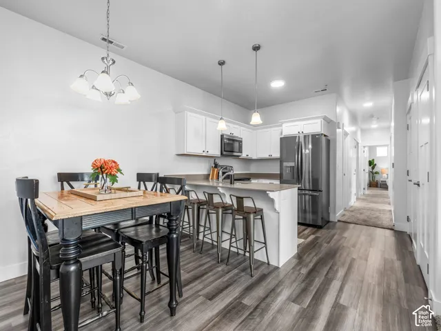 Open-concept kitchen featuring white cabinetry, stainless steel appliances, a breakfast bar, and wood-finish flooring