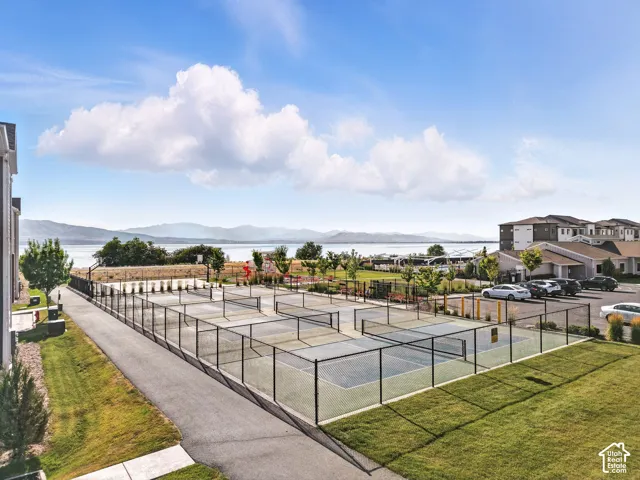 Multiple hard-surface courts with fencing, paved walkways, landscaped grounds, and a mountain and water backdrop