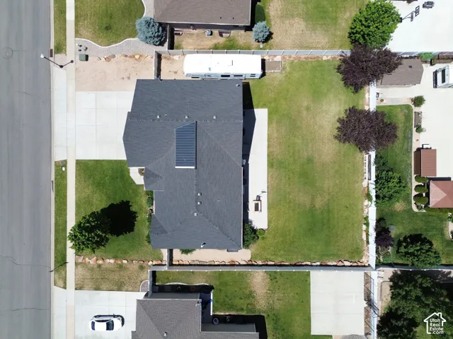 Aerial view showcasing a well-proportioned residential lot with a dark-shingle roof, solar panel array, mature landscaping including established trees, and manicured lawn space