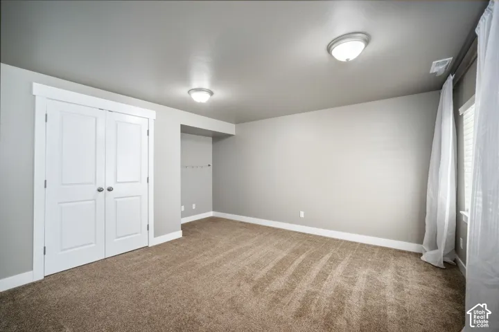 Spacious bedroom featuring neutral wall finishes, carpeted flooring with directional pattern, dual ceiling-mounted light fixtures, and a large double-door closet with white painted trim