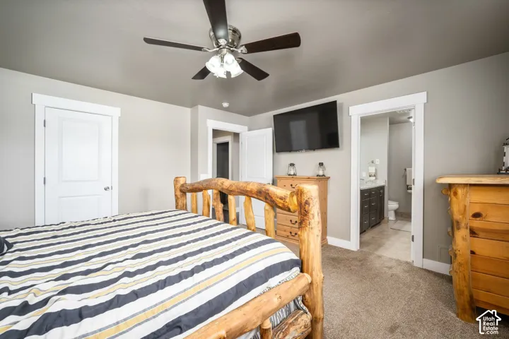 Spacious bedroom with wood-frame bed, striped bedding, carpet flooring, and ceiling fan with integrated lighting